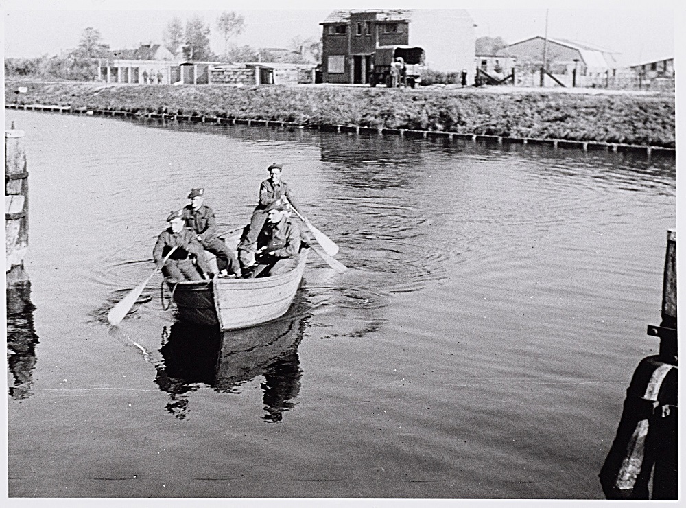 Schotse militairen steken per roeiboot het Wilhelminakanaal over nabij de vernielde draaibrug aan de Bosscheweg. Fotograaf F. Cremers
